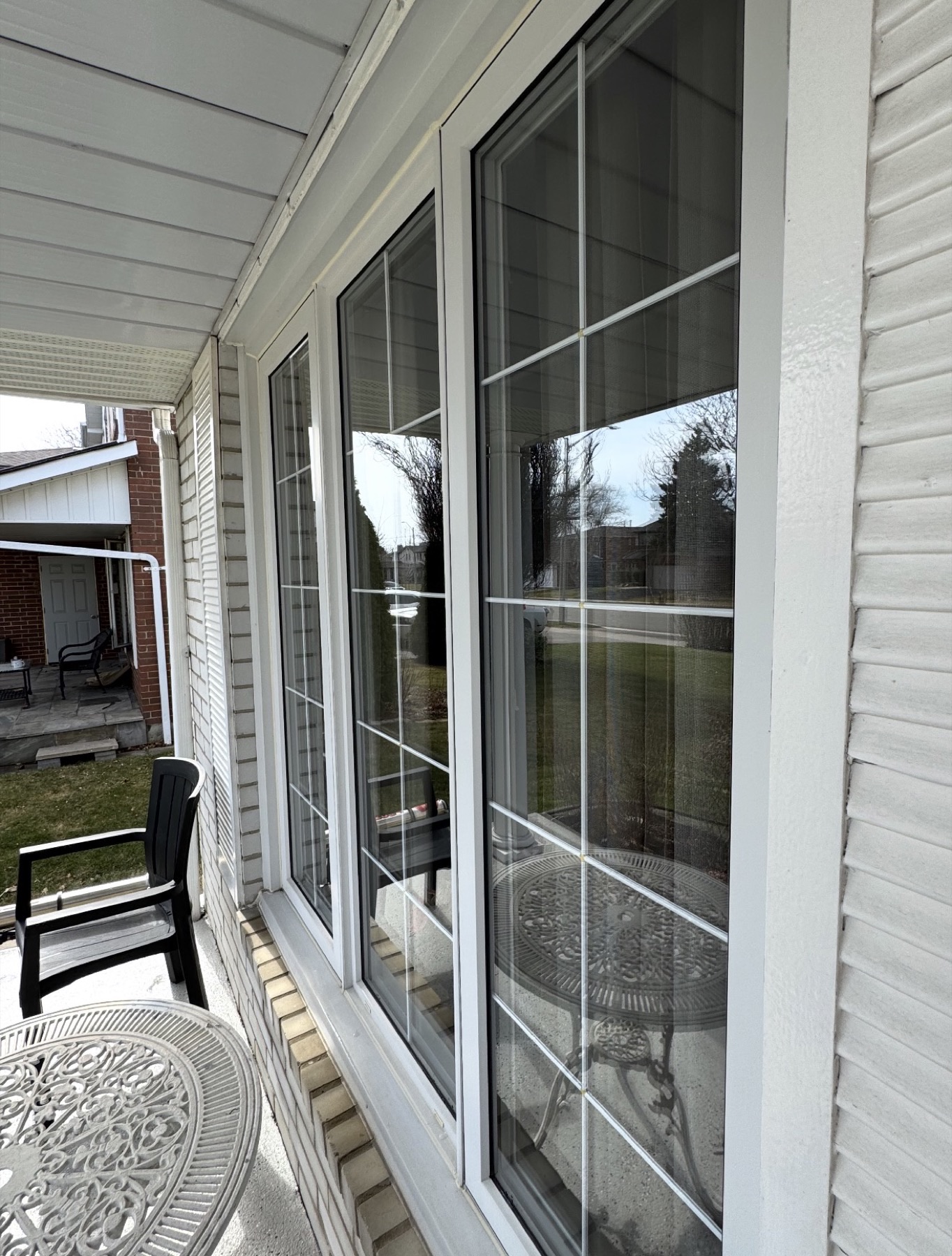 Filmed windows along a covered porch on a white-sided GTA home, the film invisible against the reflected front yard
