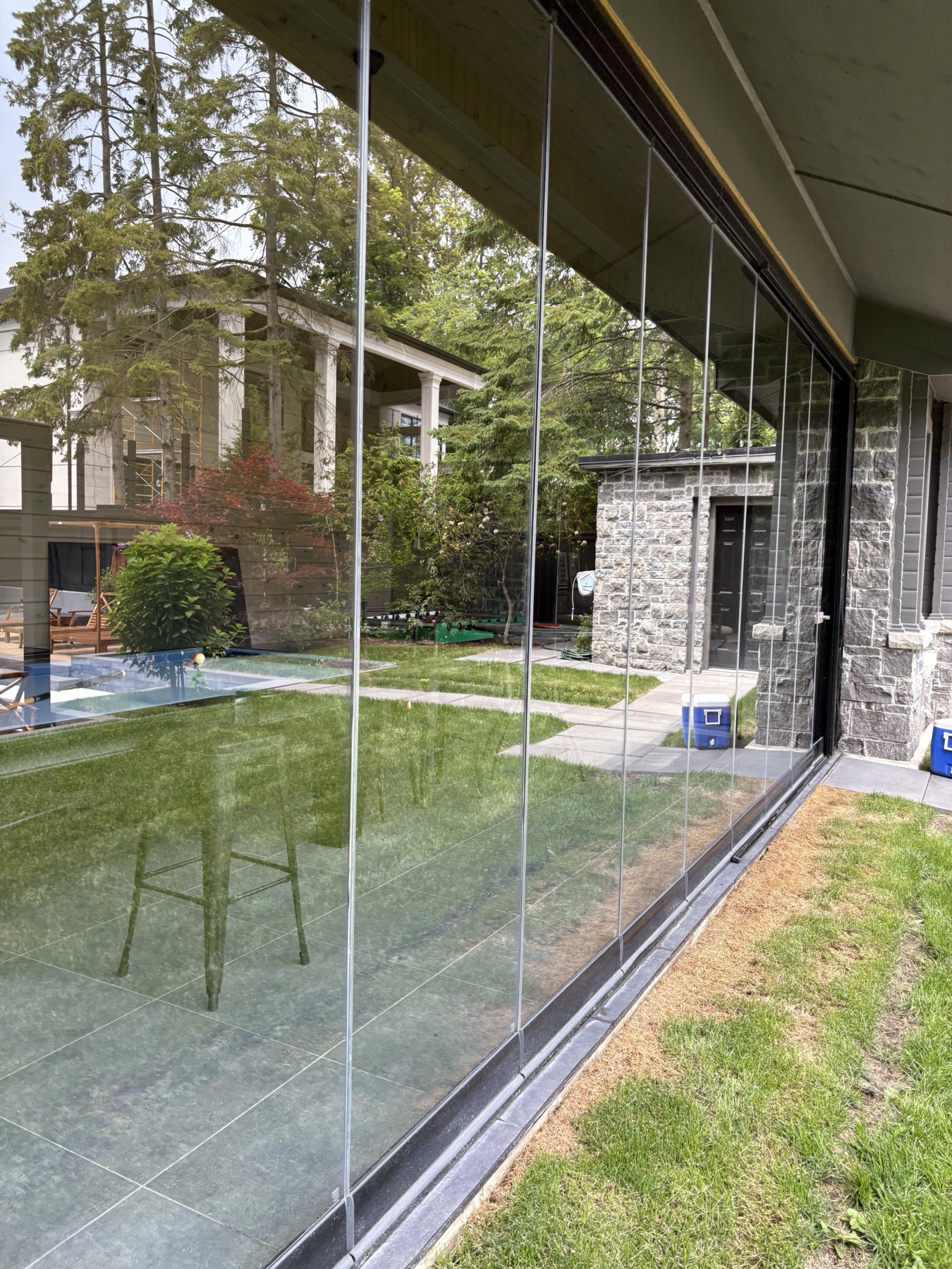 A full-height glass wall on a modern stone-clad GTA home with security film installed, looking through to the pool and garden beyond