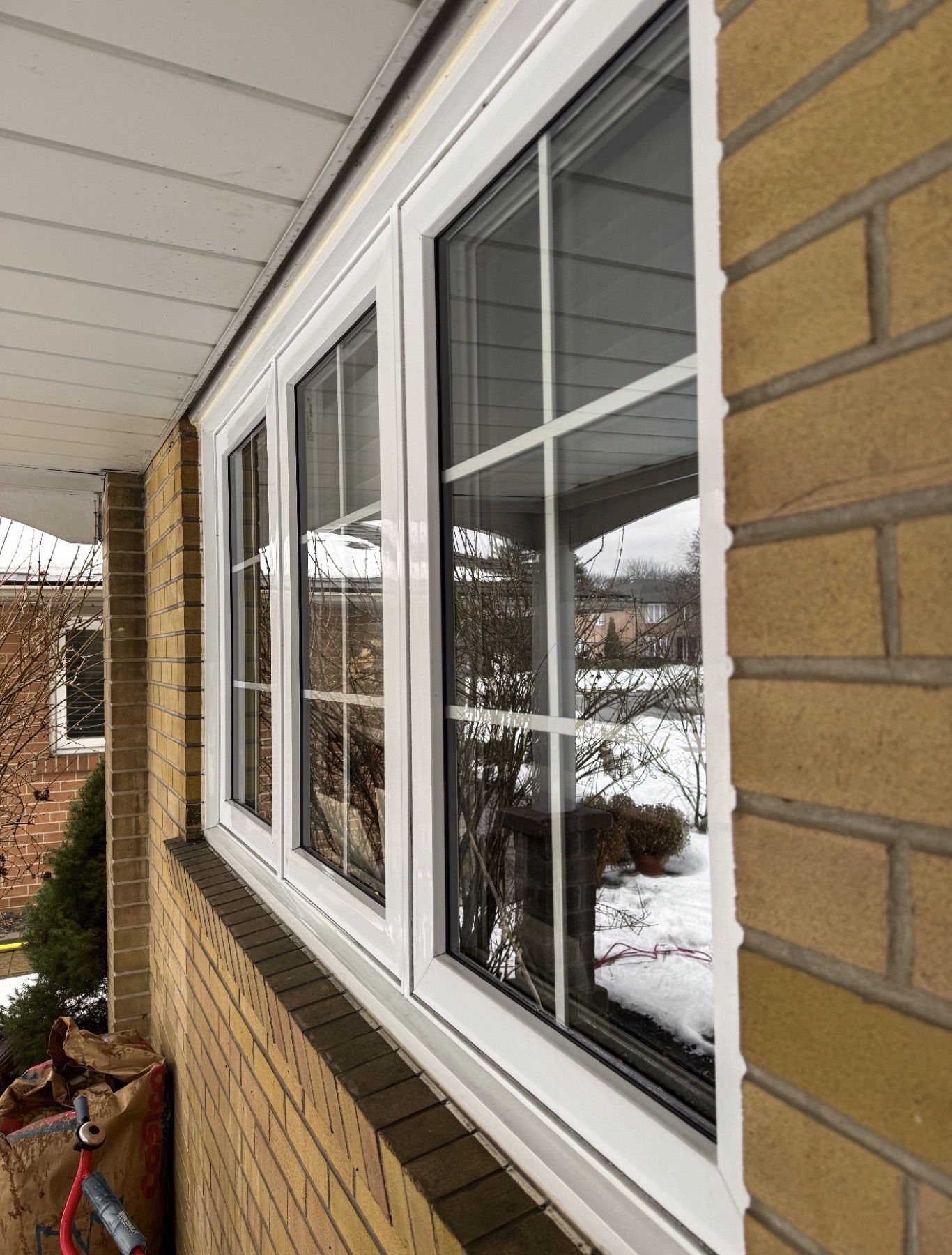 Security window film on the front windows of a yellow-brick GTA bungalow in winter, the glass optically clear with no tint or haze